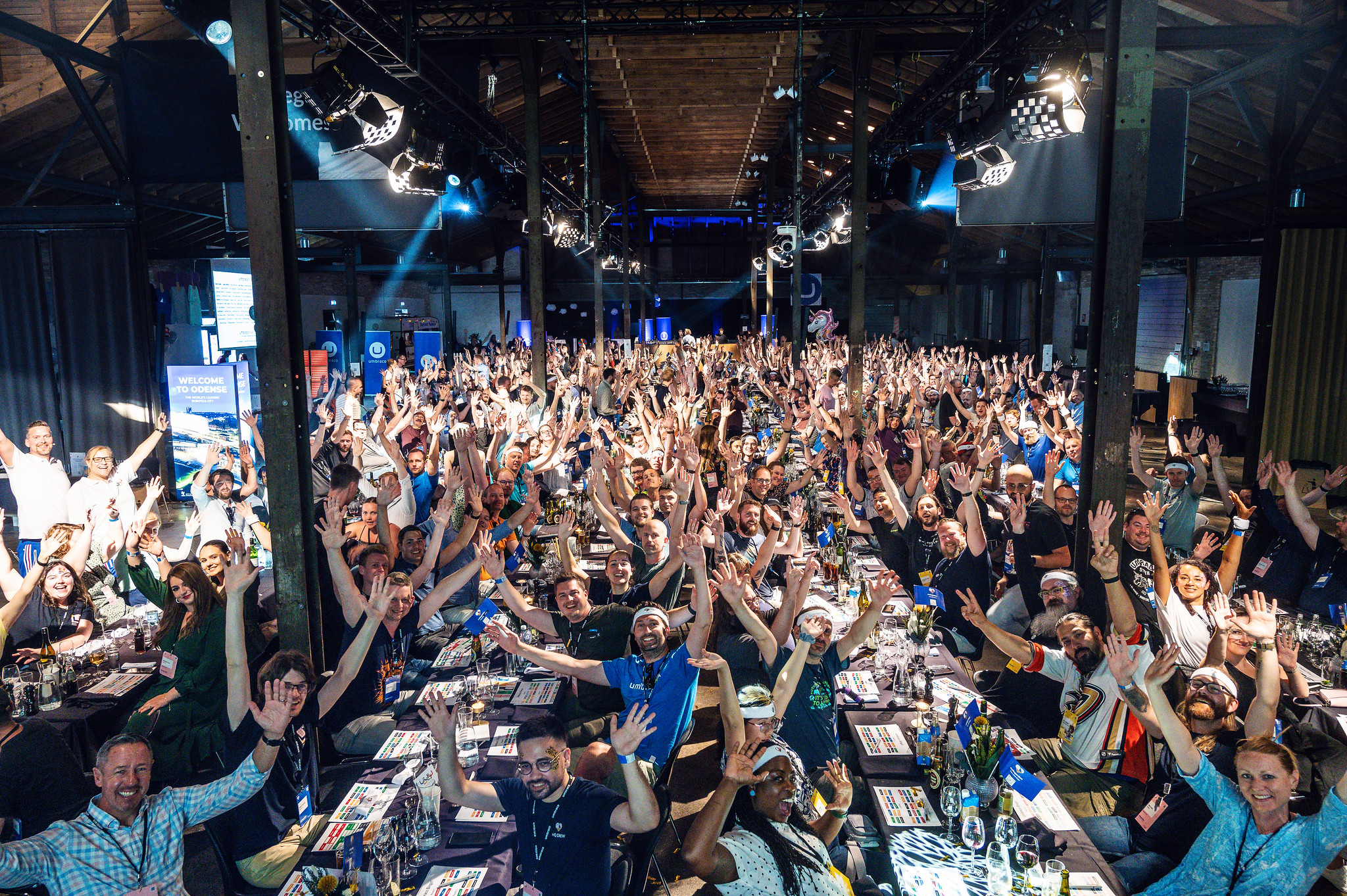 A photo by Umbraco HQ on Flickr of Codegarden 2023 attendees sat at long tables, with hands raised in the air ready to play bingo!